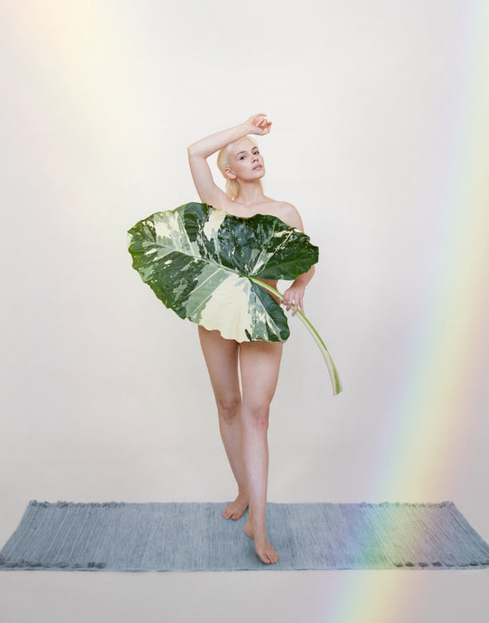 Person wearing a large leaf-like garment, standing on a yoga mat, on a plain background