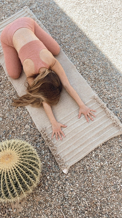 Person stretching on a textured yoga mat outdoors with a cactus plant nearby