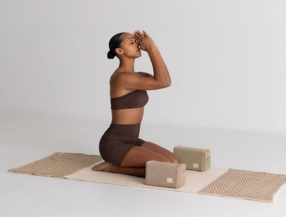 Woman in brown athletic wear practicing yoga on a mat with yoga blocks against a plain background