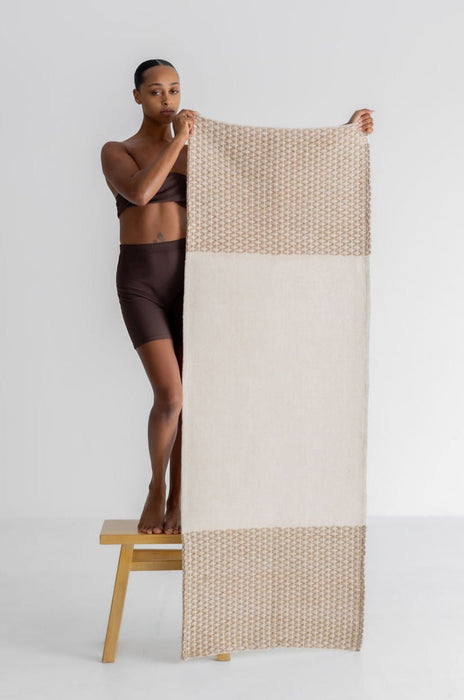 Woman holding up a yoga mat with a white and beige pattern on a white background