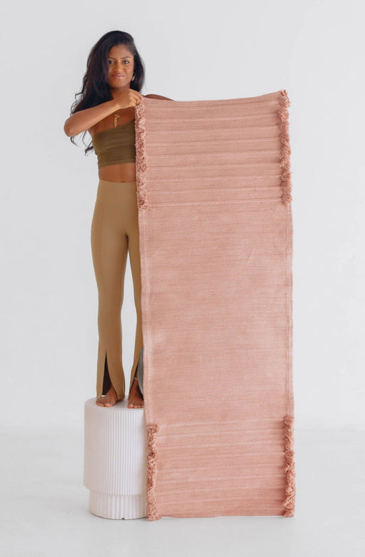 Woman holding up a pink yoga mat against a white background