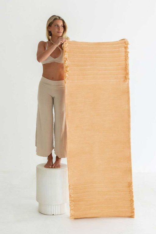 Woman holding up an orange yoga mat against a white background