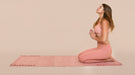 Woman in a yoga pose on a pink mat with a beige background