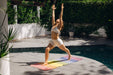 Woman practicing yoga on a colorful mat by a pool