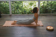 Woman practicing yoga on a mat in a serene outdoor setting with greenery.