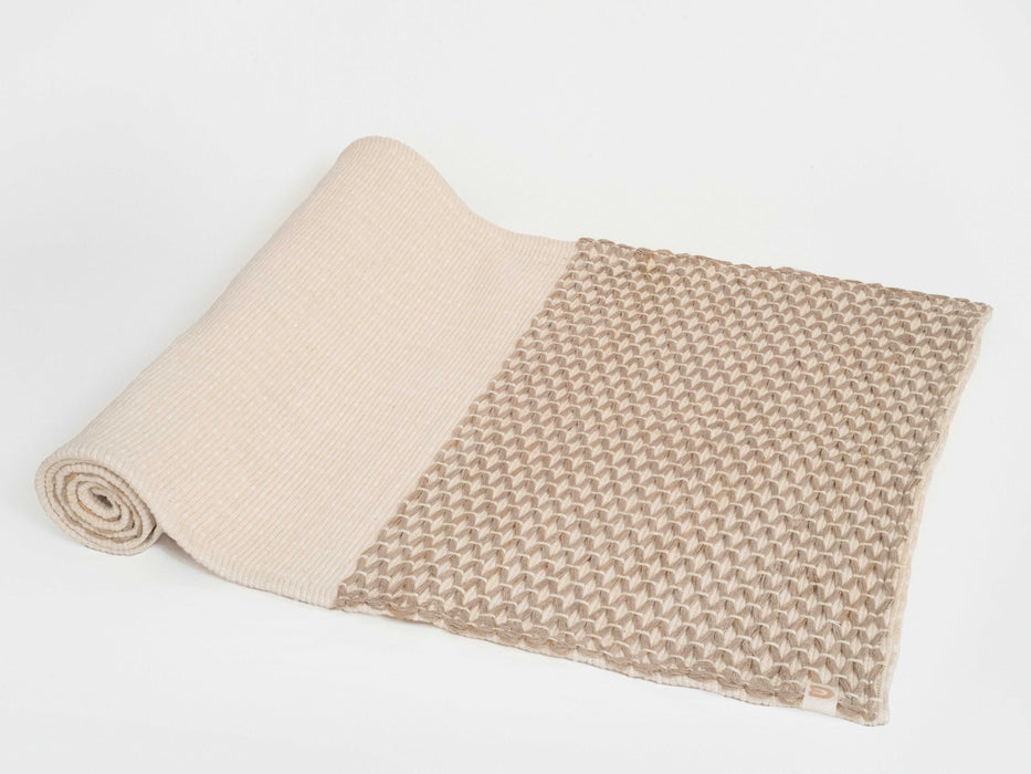 Partially unrolled beige yoga mat, showing grippy diamond pattern, on a white background