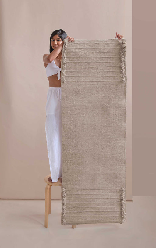 Woman standing on a stool and holding a textured yoga mat against a beige background