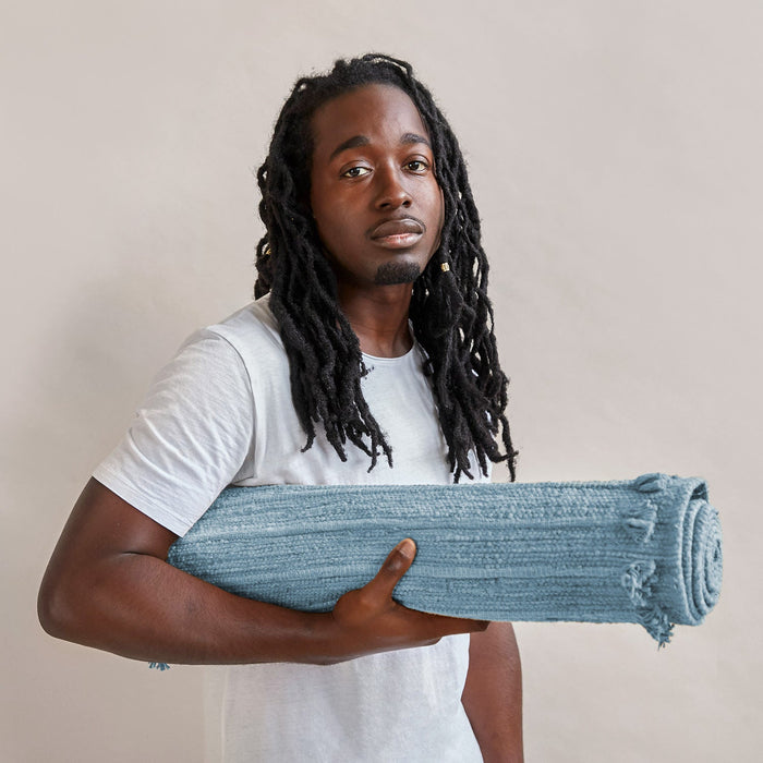 Man holding a rolled blue yoga mat against a plain background