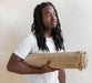 Man holding a rolled-up beige yoga mat against a plain background