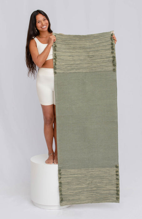Woman holding up a green yoga mat  against a plain background