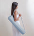 Woman holding a yoga mat in a carry case against a plain background
