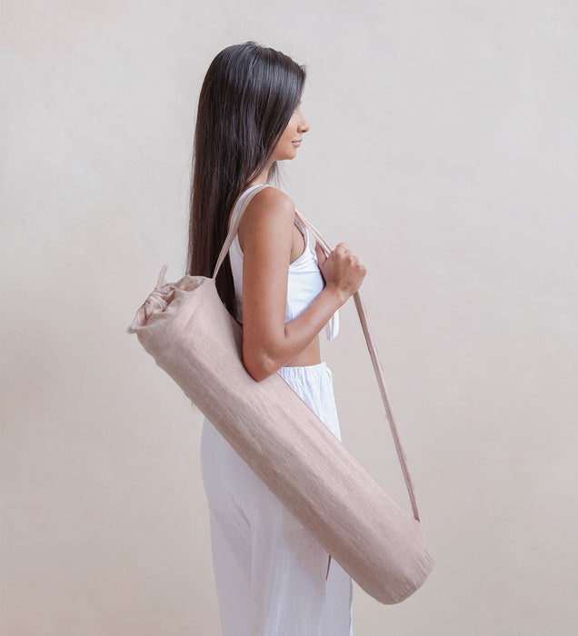 Woman holding a beige yoga mat bag against a plain background