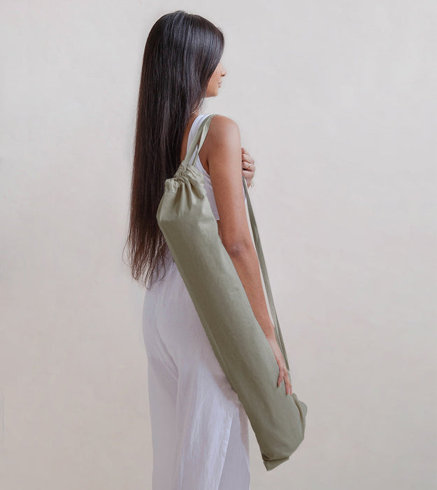 Woman holding a green yoga mat bag against a plain background