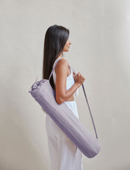 Woman holding a purple yoga mat bag against a plain background
