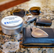 Myofascial releaser, tin of emollient , wallet, sunglasses, and other items on a marble surface