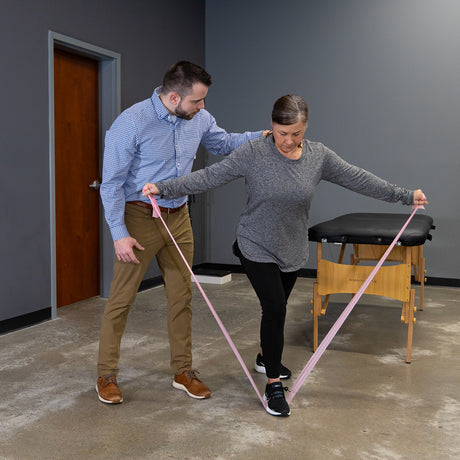 Physiotherapist assisting a patient with a resistance band in a therapy room.