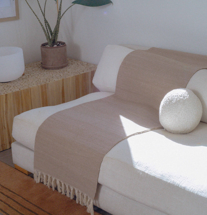 Beige yoga mat with tassles draped over a white sofa with a plant and decorative ball in the background.