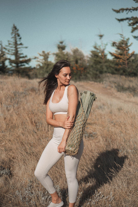 Woman in athletic wear holding a yoga mat in a bag in a natural setting