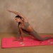 Woman in a yoga pose on a pink mat with a neutral background