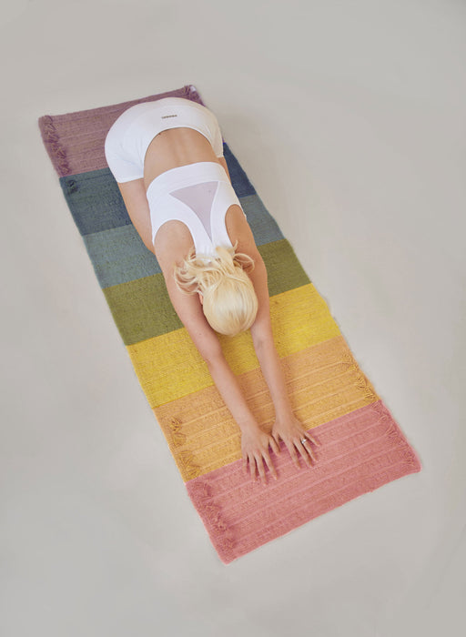 Person in a yoga childs pose on a rainbow striped yoga mat. 