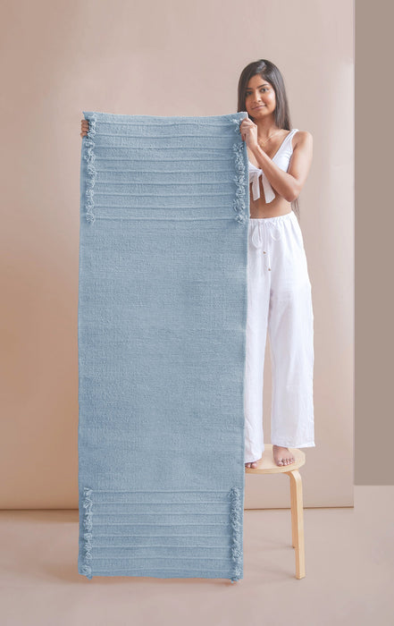 Woman holding up a blue yoga mat against a beige wall.