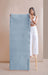 Woman holding up a blue yoga mat against a beige wall.