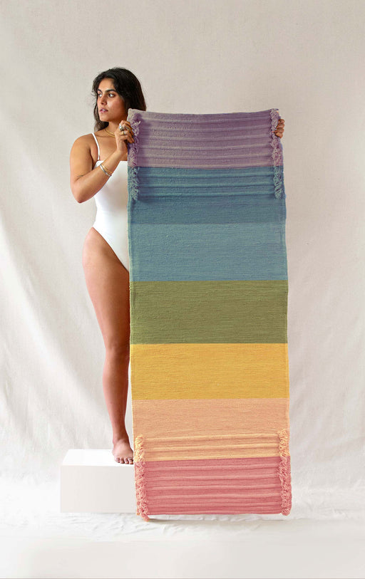 Woman holding up a colorful yoga mat against a plain background